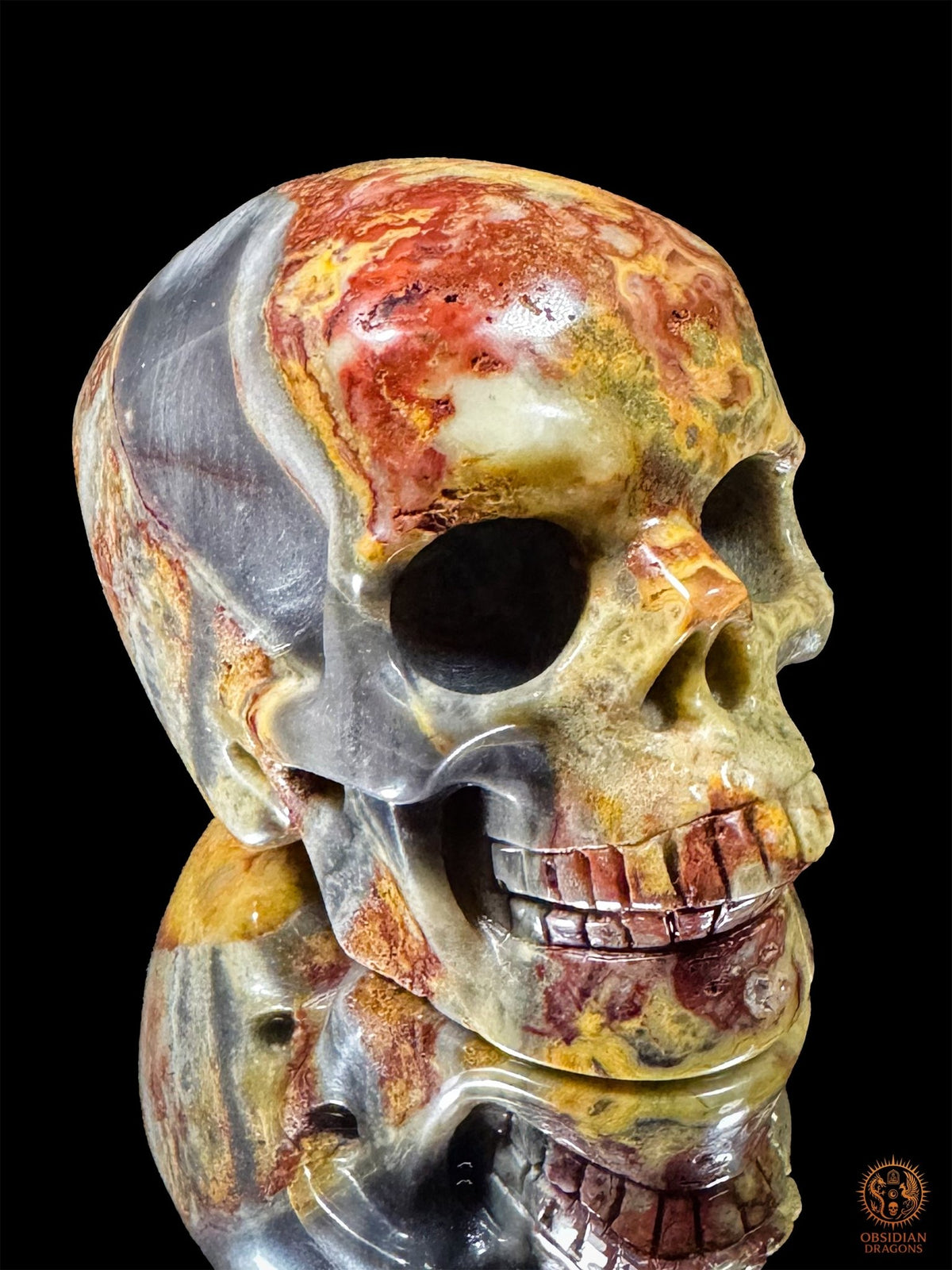 Crâne en jaspe polychrome de Madagascar vu de trois quarts, avec une tempe grise, un front rouge et crème et une mâchoire polie.