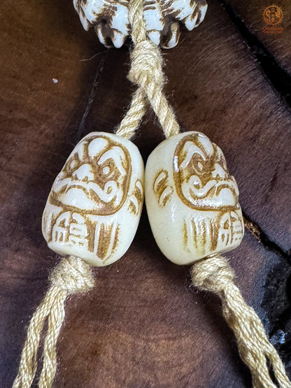 Deux perles terminales Daruma représentant Bodhidharma, sculptées en bois de cerf et montées sur un cordon blanc