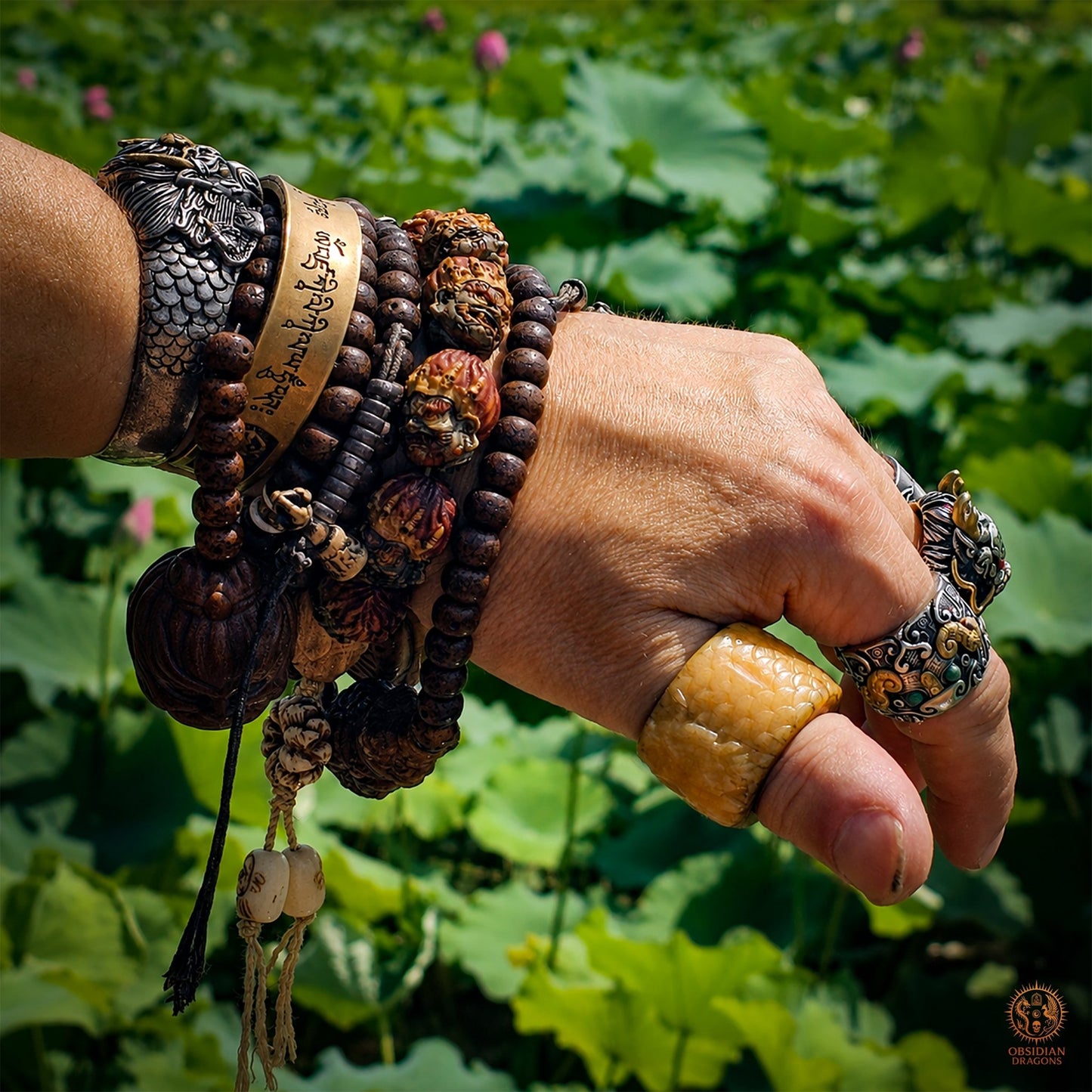 Bracelet mala Mahakala porté au poignet parmi des bijoux bouddhistes, avec perles en bois de cerf devant un jardin de lotus