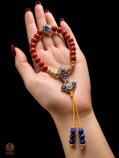 Bracelet mala Shibazi 18 perles en agate Nan Hong de Baoshan, cloisonné doré et lapis-lazuli, présenté dans une main - Obsidian Dragons