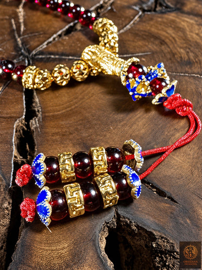 Finitions du bracelet Shibazi : deux brins rouges ornés de grenats, de fleurs cloisonnées bleues et d’intercalaires en bronze plaqué or.