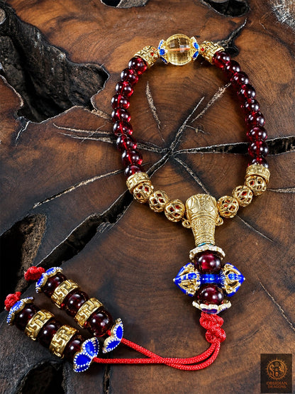 Bracelet mala en grenat et citrine vu de dessus sur bois, avec perle de Guru dorée, dorje cloisonné bleu et nœud coulissant rouge.