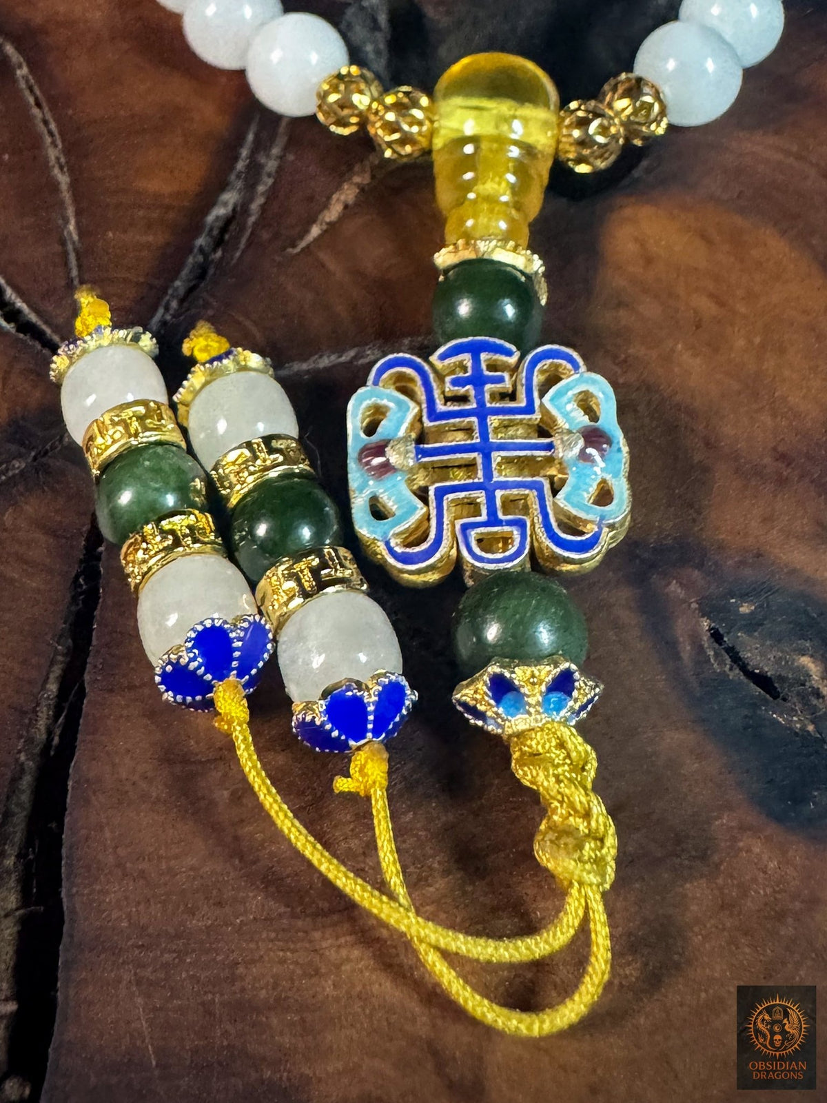 Gros plan sur le motif shòu en émail cloisonné, la perle de guru en ambre et les deux terminaisons en jade du bracelet mala.