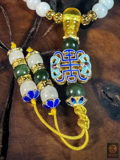 Gros plan sur le motif shòu en émail cloisonné, la perle de guru en ambre et les deux terminaisons en jade du bracelet mala.