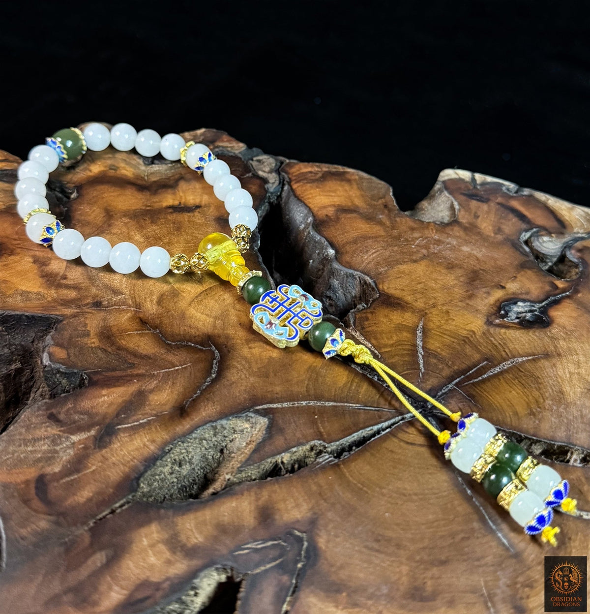 Bracelet mala en jade blanc et vert disposé sur du bois, montrant l’ambre, le symbole shòu et son cordon jaune réglable.