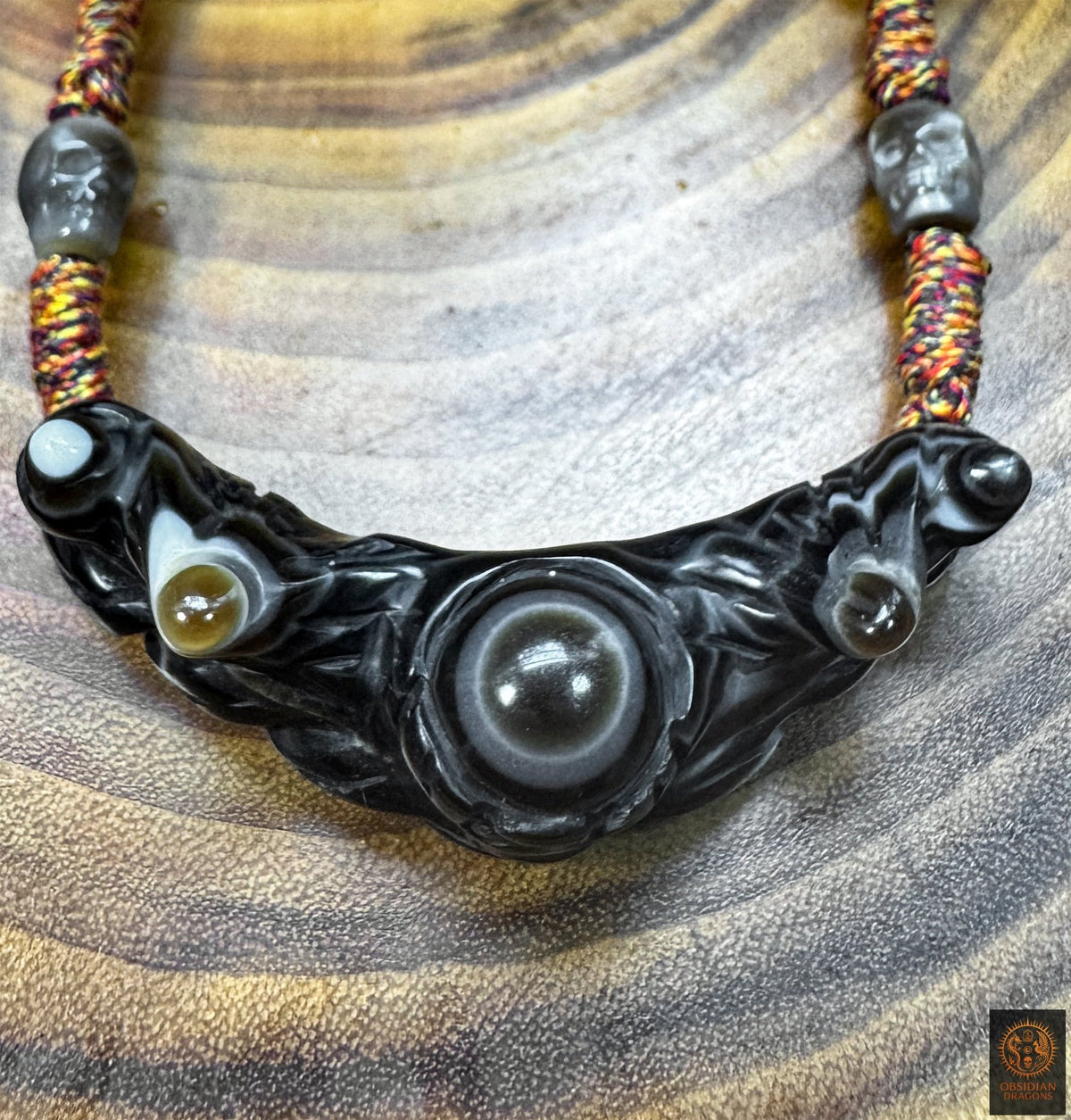 Gros plan du pendentif Lug Mig en agate oculaire noire, œil magique tibétain aux structures naturelles concentriques sculptées.