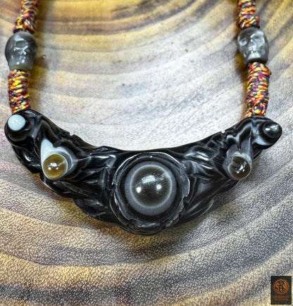 Gros plan du pendentif Lug Mig en agate oculaire noire, œil magique tibétain aux structures naturelles concentriques sculptées.