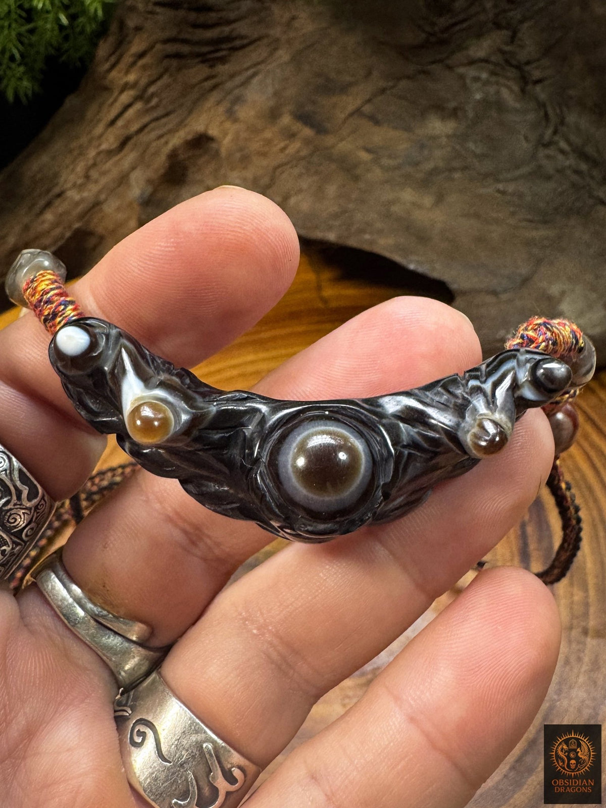 Pendentif Lug Mig tibétain en agate sculptée tenu en main, grand œil naturel central et formations orbiculaires secondaires.