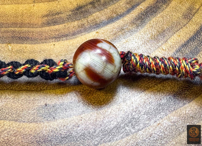 Détail d’une perle Dzi "crochet de fortune" en agate du collier de protection tibétain Lug Mig, montée sur tressage artisanal noir rouge et or.