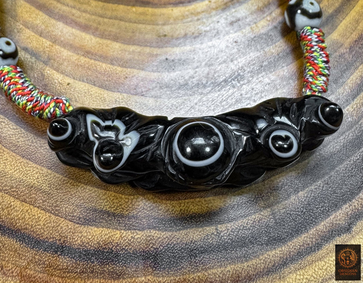Gros plan du pendentif Lug Mig traditionnel en agate oculaire, pierre Œil céleste sculptée aux multiples motifs naturels en forme d’yeux.