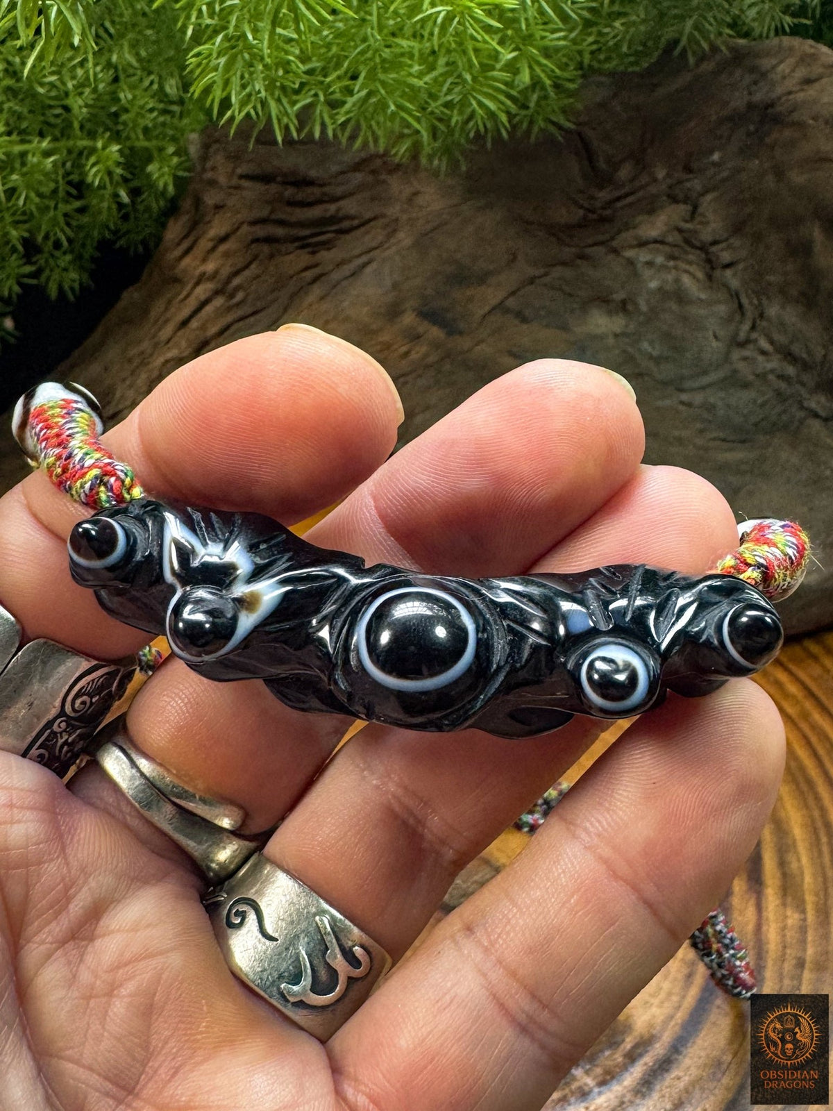 Pendentif Lug Mig tibétain tenu en main, agate noire sculptée avec grand œil naturel central et structures oculaires secondaires.
