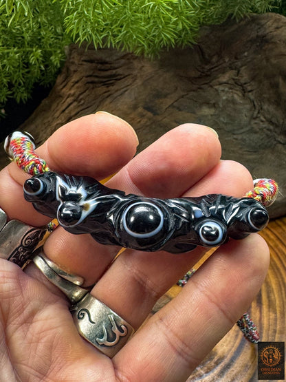 Pendentif Lug Mig tibétain tenu en main, agate noire sculptée avec grand œil naturel central et structures oculaires secondaires.