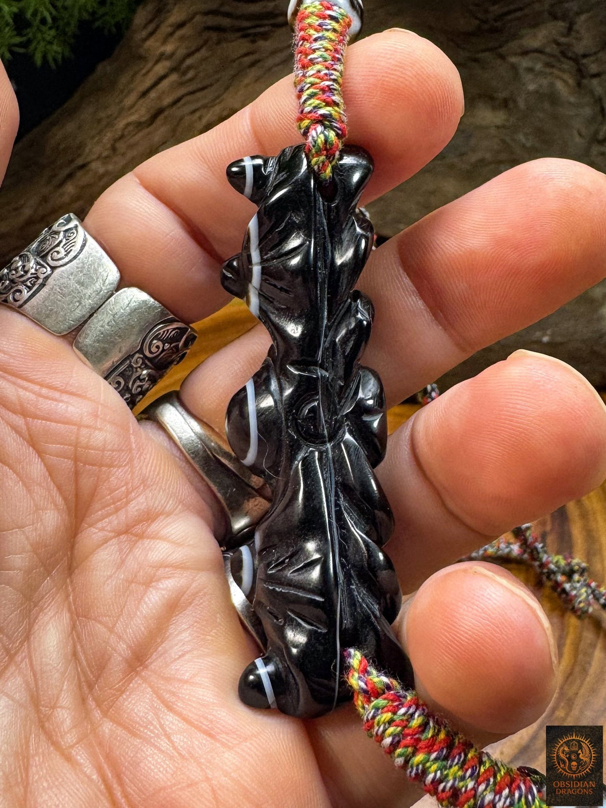 Vue latérale du pendentif œil magique tibétain Lug Mig, sculpture profonde en agate noire et montage sur cordon artisanal multicolore.