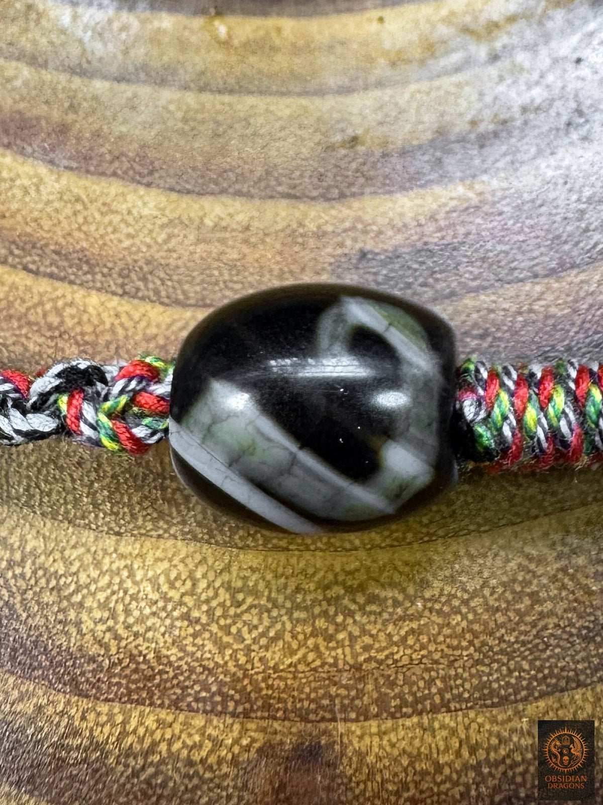 Gros plan d’une perle Dzi tibétaine  Tara du collier œil magique Lug Mig, montée sur tressage artisanal multicolore en coton.