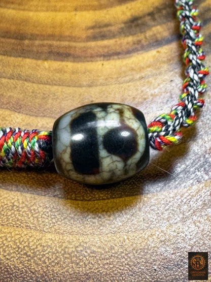 Détail d’une seconde perle Dzi tibétaine monseigneur, du collier Lug Mig traditionnel, agate noire et claire montée sur cordon tressé artisanal.