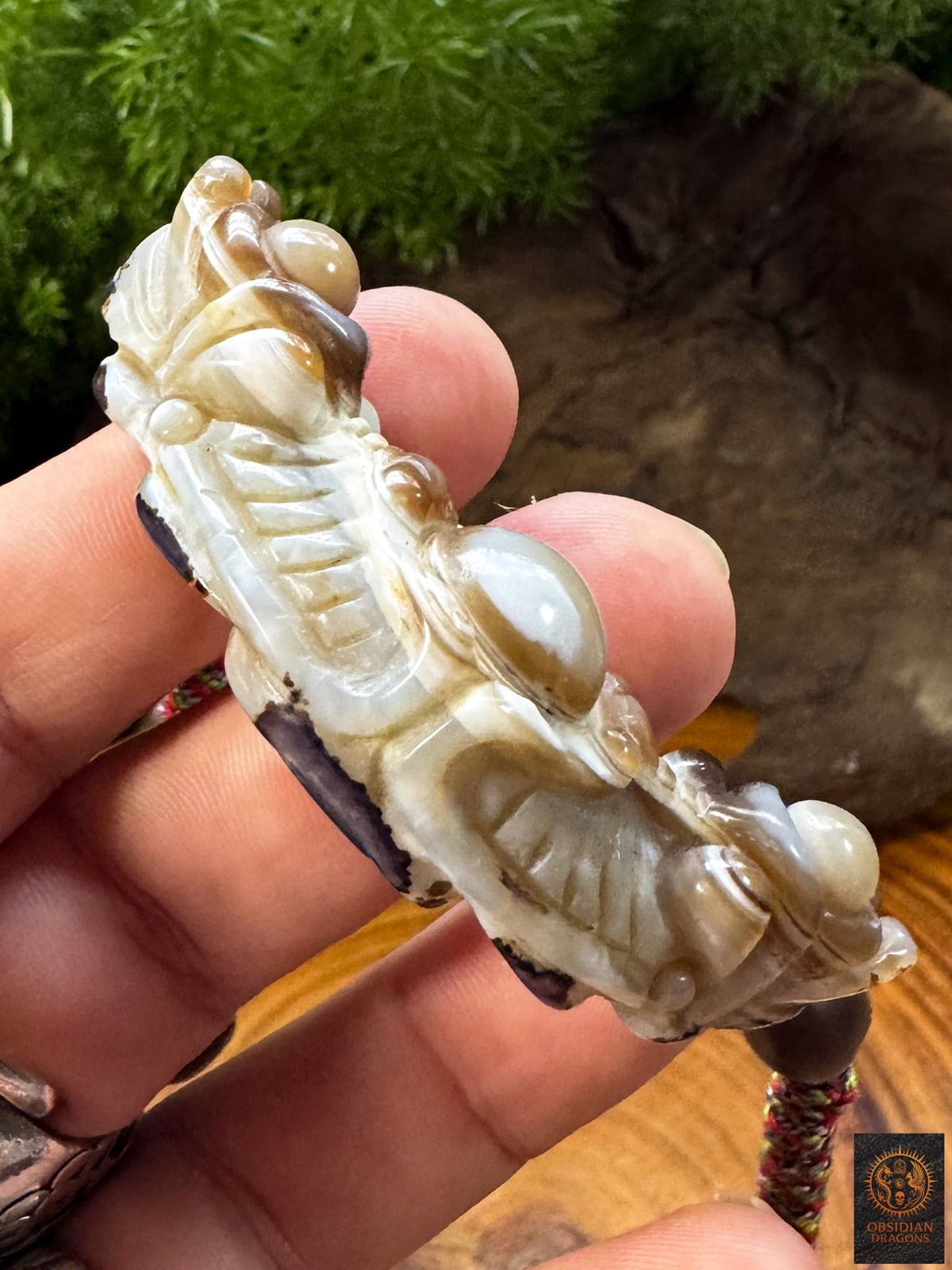 Vue de profil du pendentif Lug Mig en agate naturelle montrant son épaisseur, sa sculpture en relief et les motifs de la pierre Œil céleste