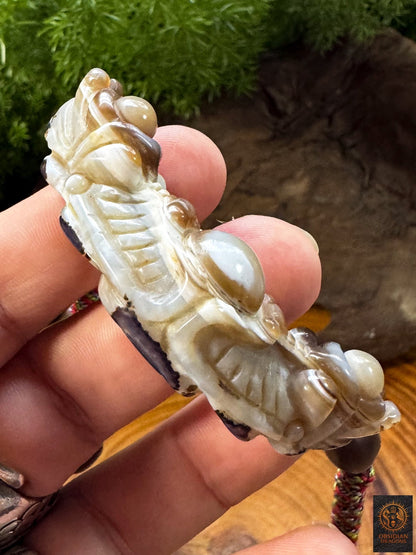 Vue de profil du pendentif Lug Mig en agate naturelle montrant son épaisseur, sa sculpture en relief et les motifs de la pierre Œil céleste