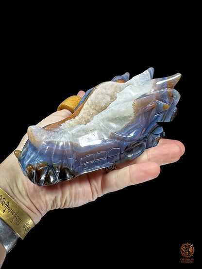 Crâne de dragon artisanal en agate et quartz tenu dans la main, vue trois quarts montrant son format de 15 cm et sa cavité cristalline - Obsidian Dragons