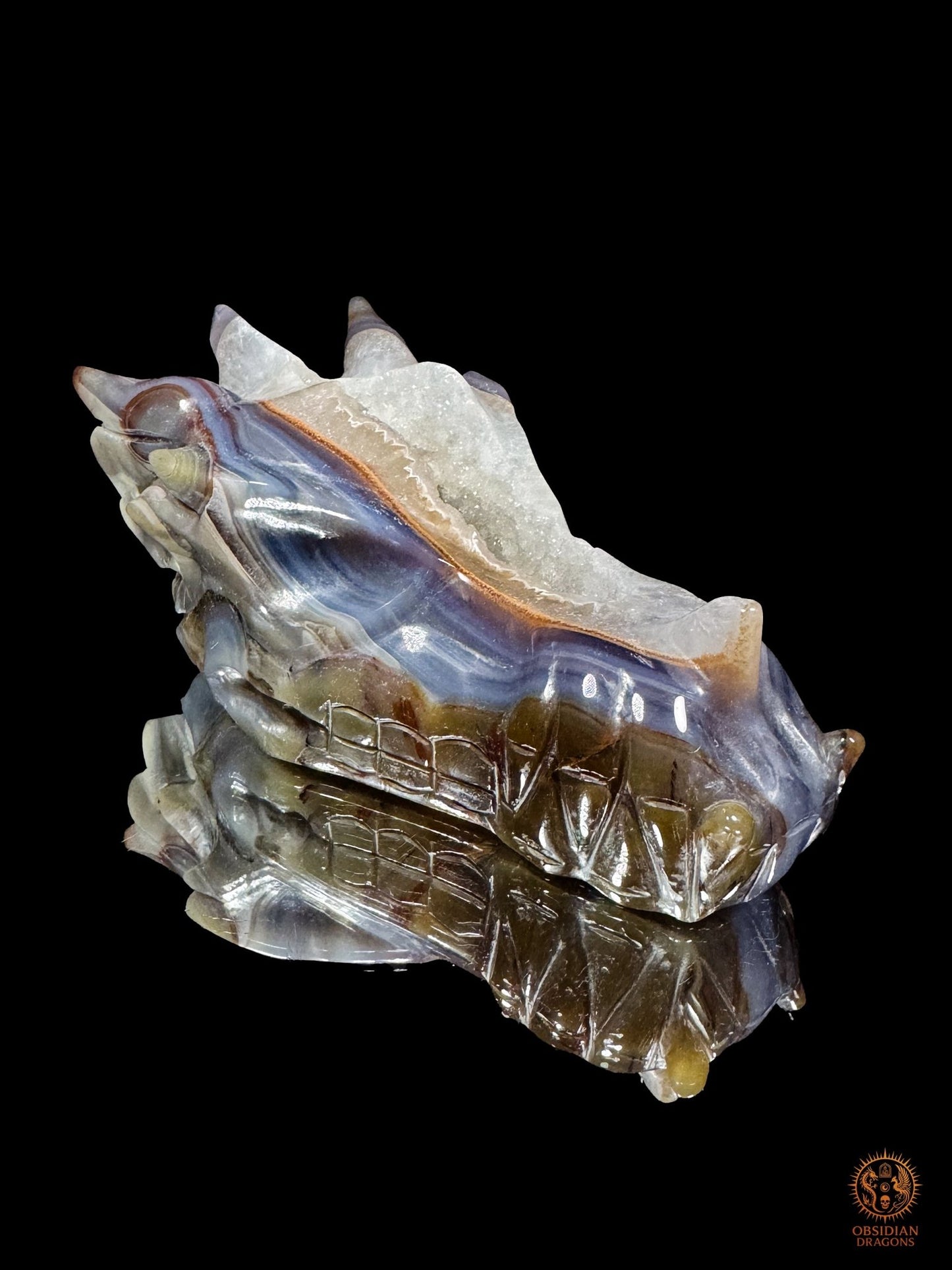 Vue latérale du crâne de dragon en géode de quartz, avec orbite profonde, mâchoire sculptée et bandes d’agate bleu-lavande
