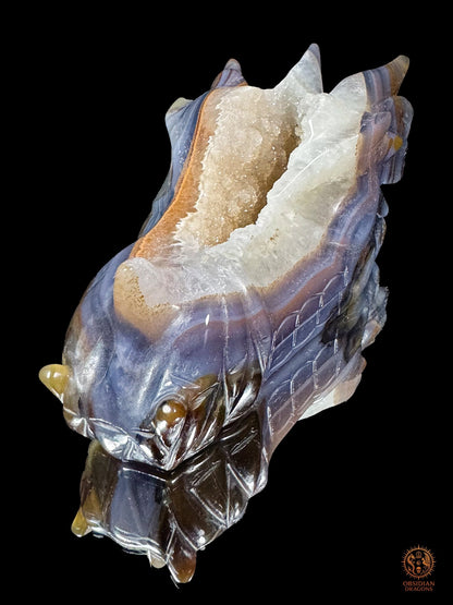 Crâne de dragon en agate rubanée et cristal de roche, vue plongeante mettant en valeur la faille minérale ouverte entre les cornes
