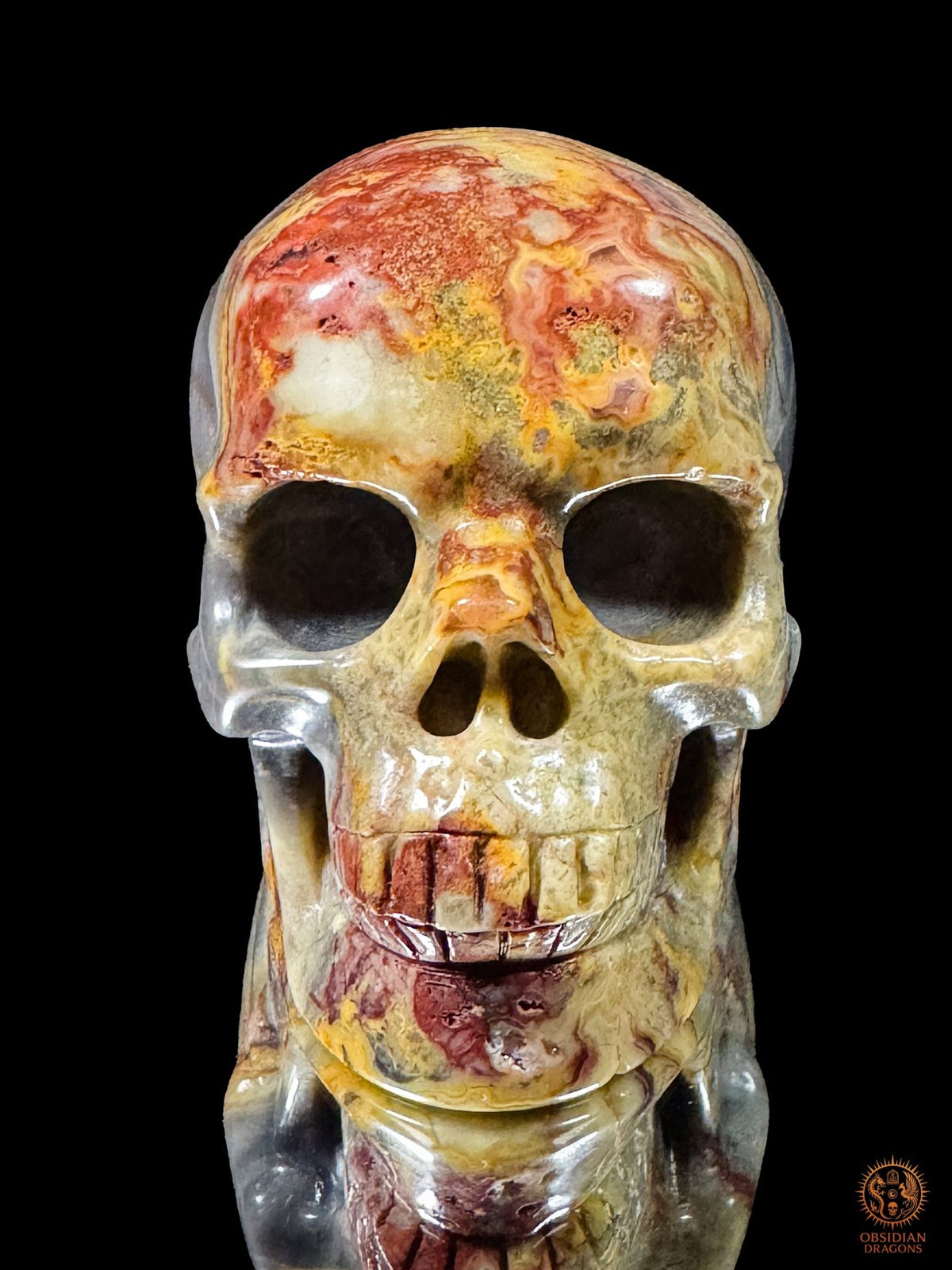 Vue de face d’un crâne en jaspe polychrome sculpté à la main, au front rouge et ocre et à la dentition multicolore - Obsidian Dragons
