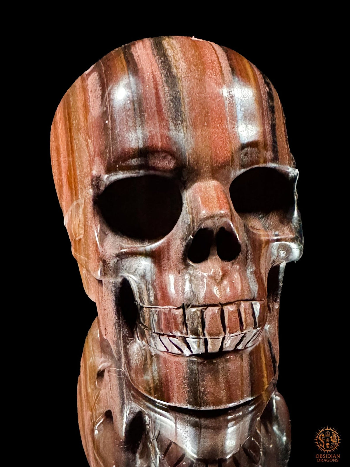 Crâne en œil de fer vu presque de face, avec des bandes verticales sur le front, des pommettes polies et des dents sculptées.