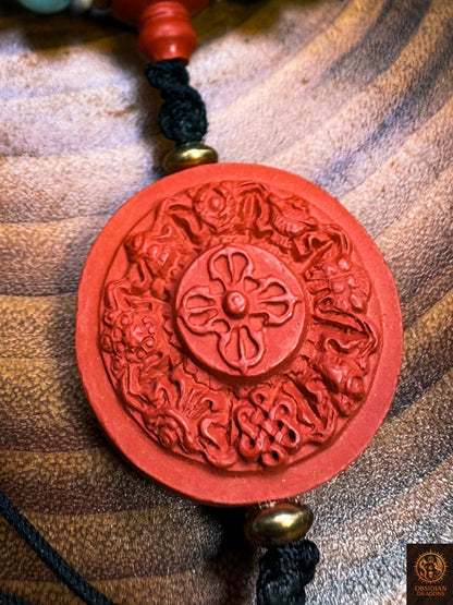 Gros plan du pendentif en cinabre sculpté d’un dorje entouré des huit symboles auspicieux du bouddhisme
