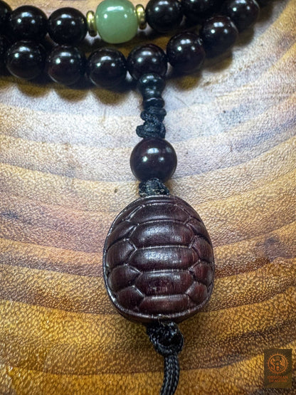 Gros plan sur la carapace de tortue en santal rouge, les nœuds du montage artisanal et une contreperle en jade de Hetian