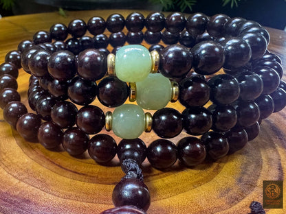 Trois contreperles en jade néphrite de Hetian encadrées de cuivre parmi les grains polis du mala en santal rouge d’Inde
