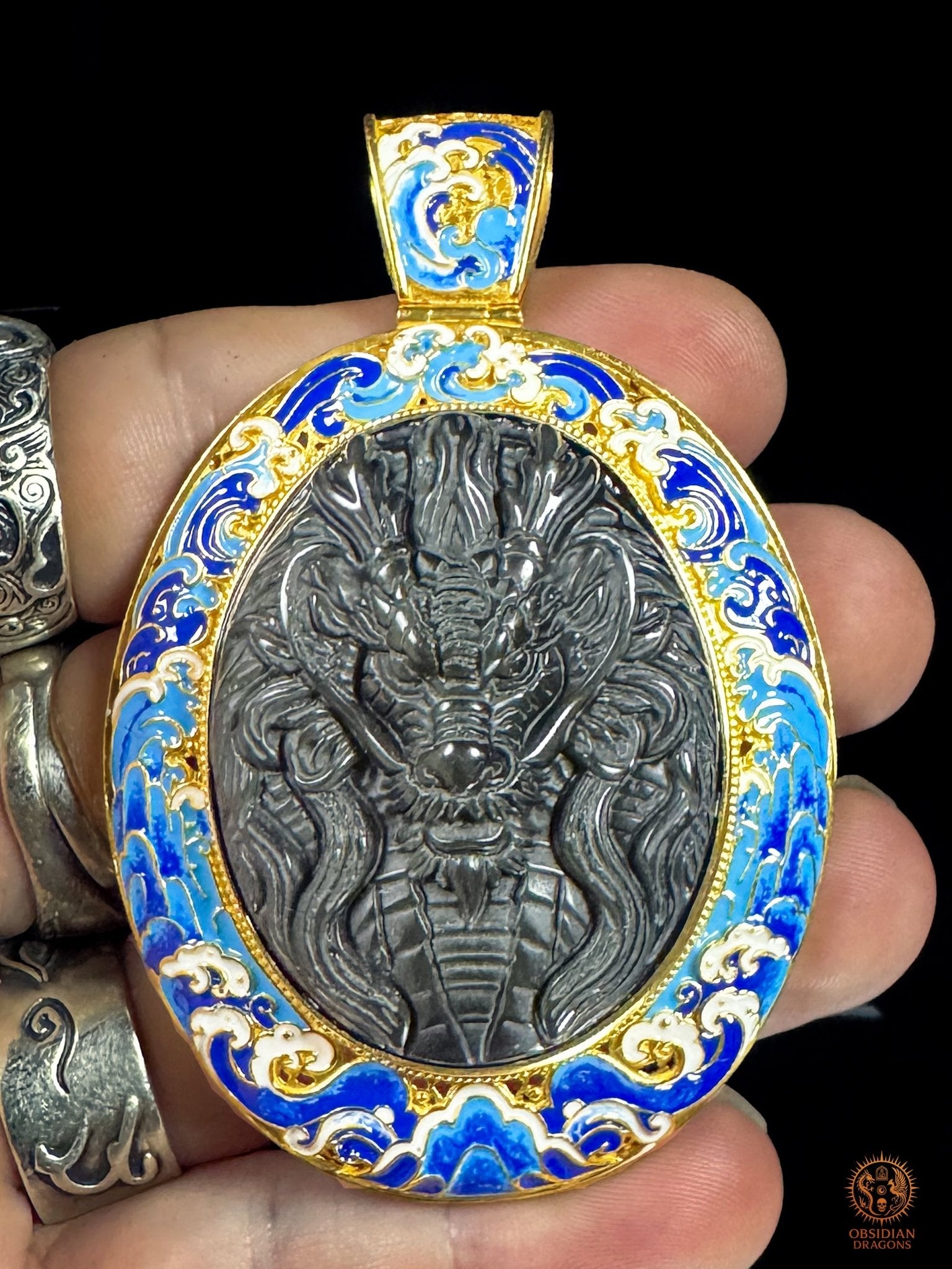 Pendentif dragon en obsidienne œil céleste tenu en main, montrant ses dimensions et son décor de vagues en cloisonné