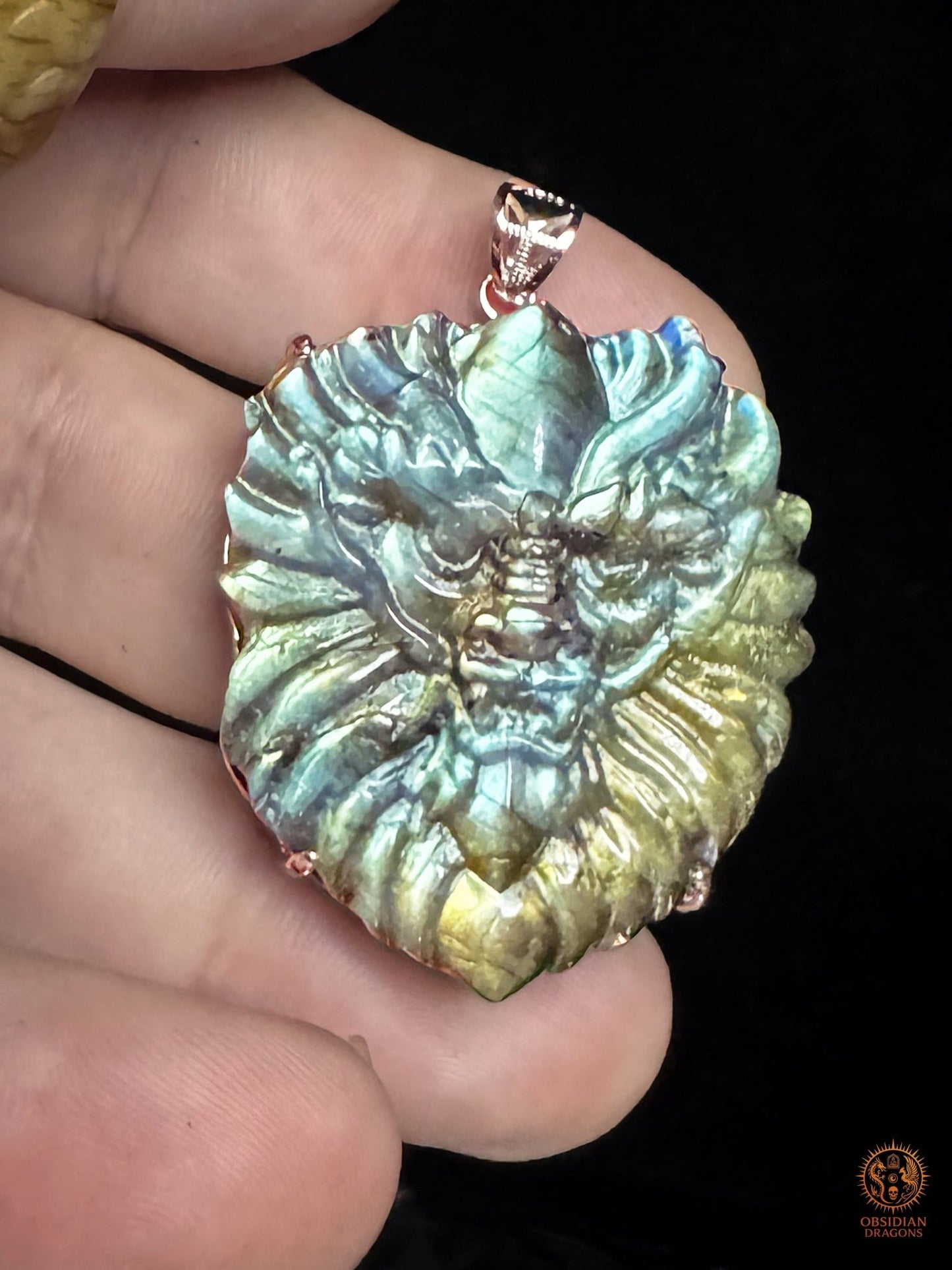 Pendentif tête de dragon en labradorite tenu en main, montrant ses dimensions, sa labradorescence et sa monture en argent 925 - Obsidian-dragons.com