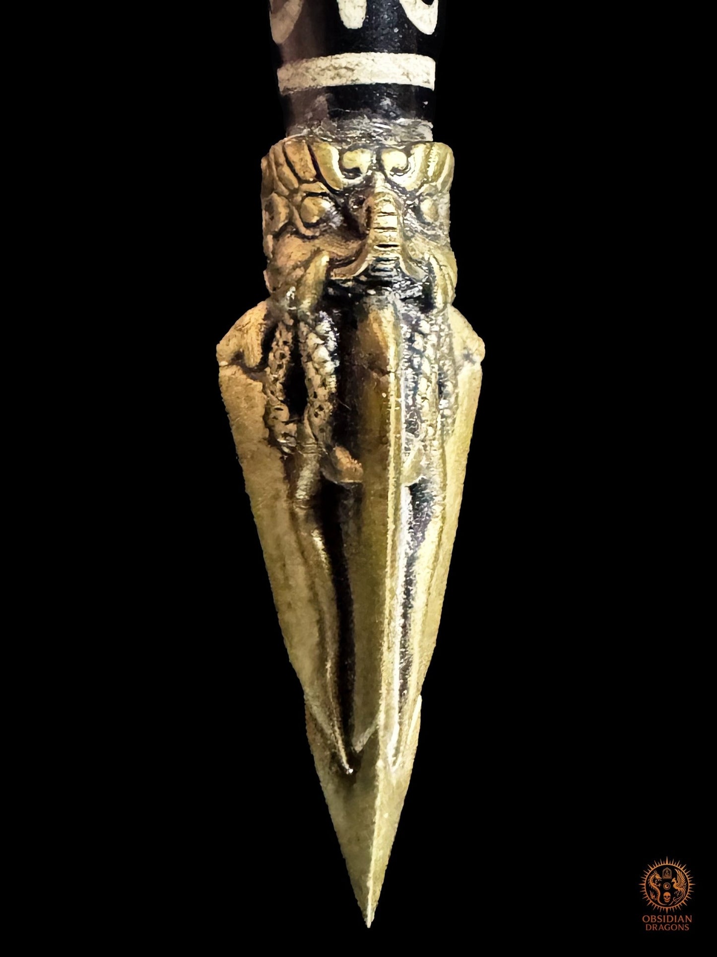 Gros plan sur une face de la lame tripartite en bronze du Phurba ornée d’un motif serpentiforme en relief