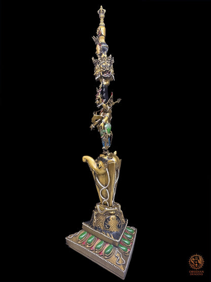 Vue trois-quarts du phurba tibétain monumental en bronze avec socle triangulaire, lame rituelle, makara et iconographie bouddhiste vajrayana