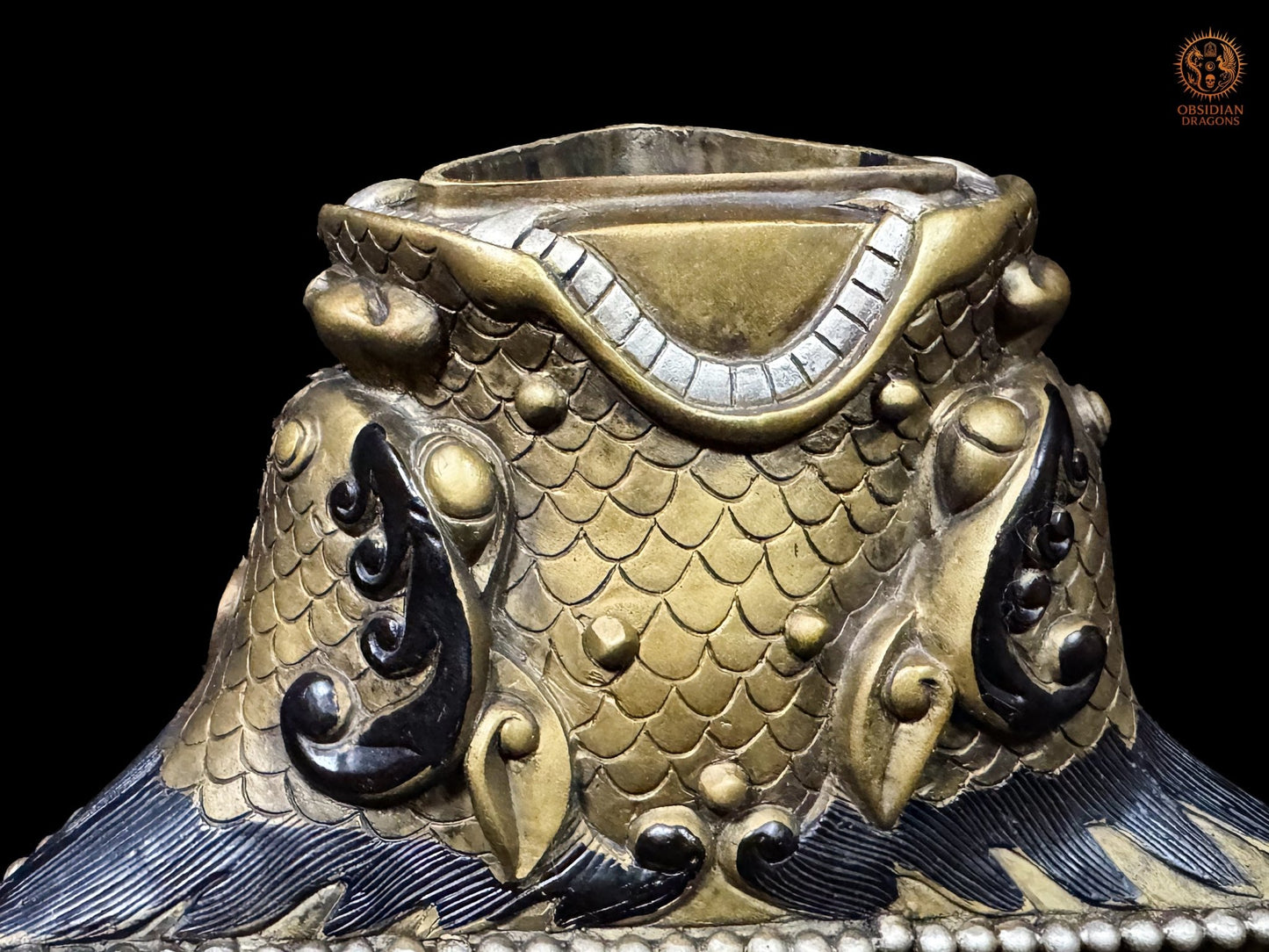 Détail du socle du phurba tibétain en bronze, décor d’écailles et faces monstrueuses symbolisant les forces et obstacles à subjuguer