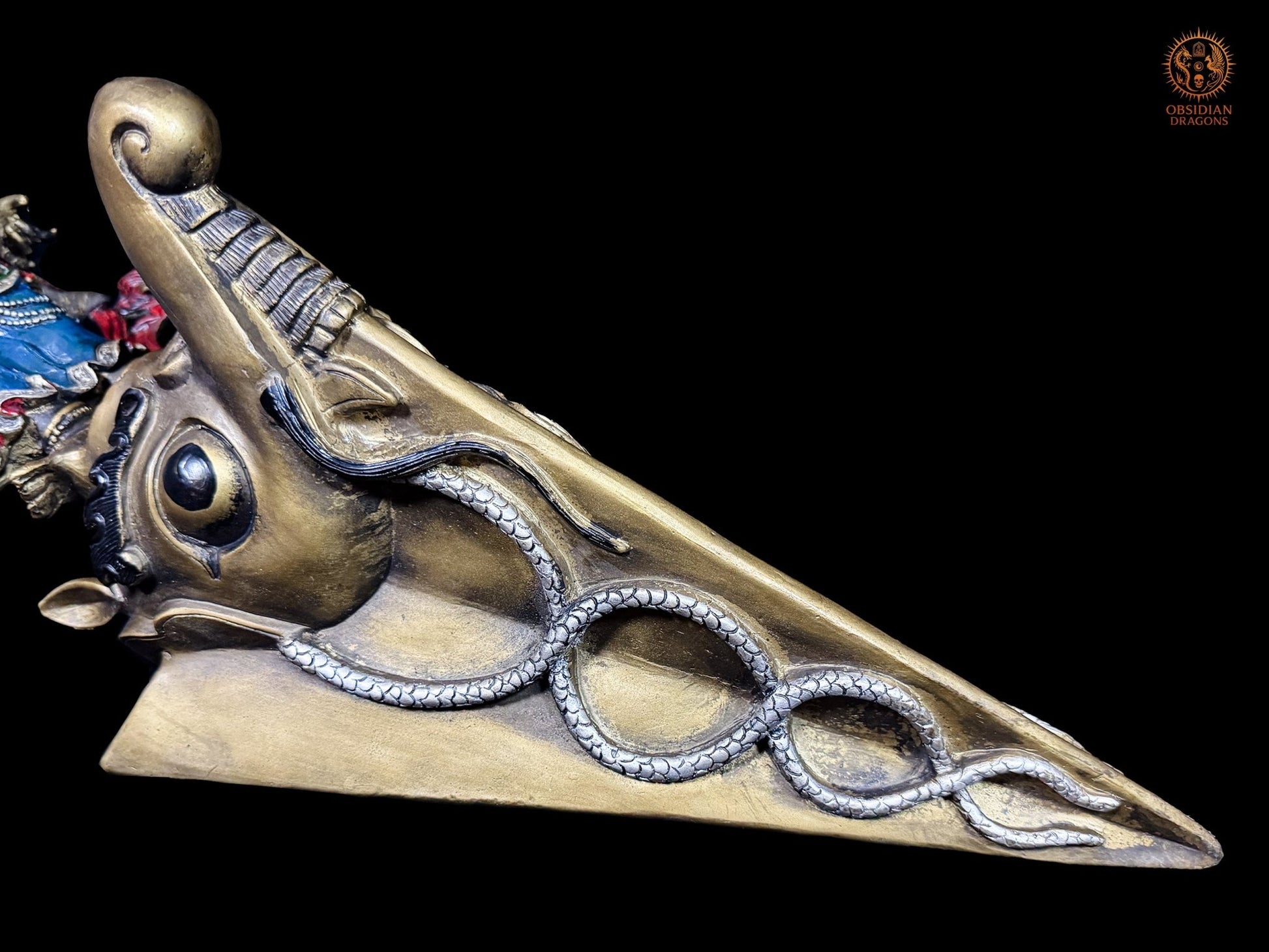 Détail de la lame du phurba tibétain en bronze avec makara et nāga entrelacés, symboles de l’iconographie bouddhiste vajrayana