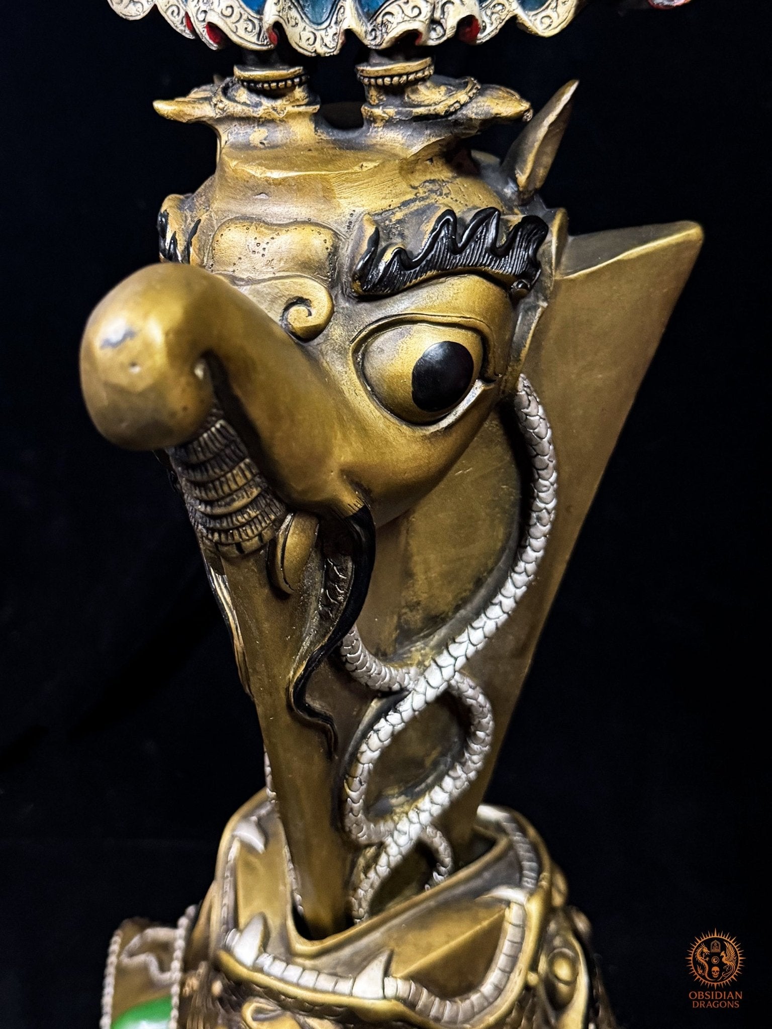 Gros plan du makara sculpté sur le phurba tibétain monumental, créature mythologique vajrayana entourée de nāga sur la lame rituelle
