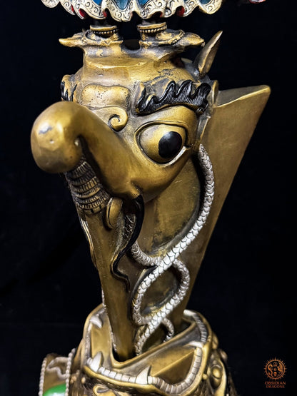 Gros plan du makara sculpté sur le phurba tibétain monumental, créature mythologique vajrayana entourée de nāga sur la lame rituelle