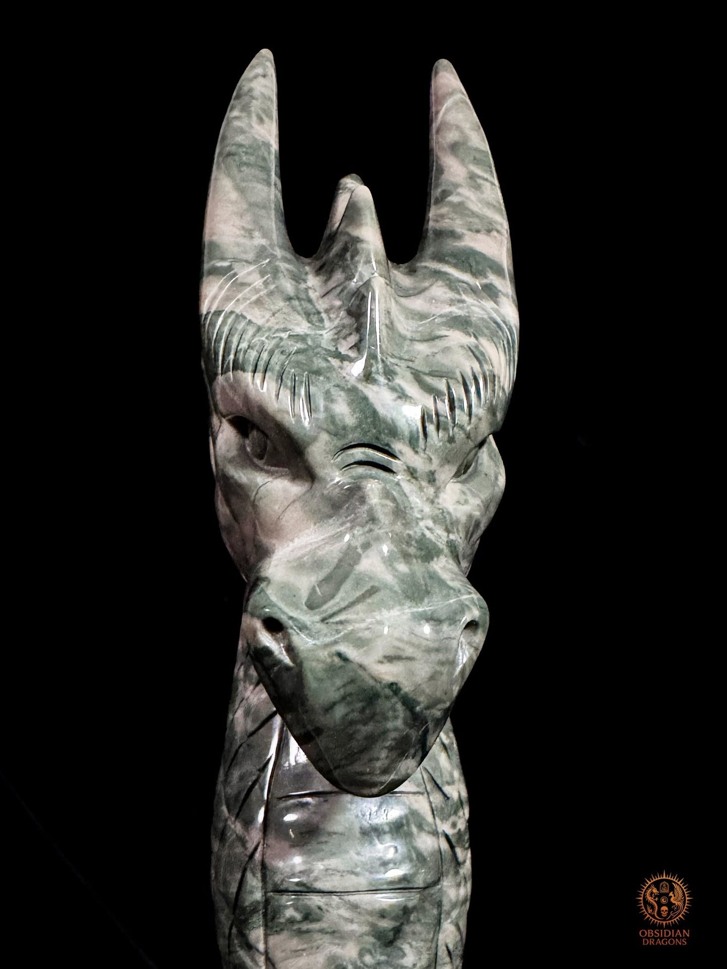 Gros plan frontal du dragon en jade des Neuf Dragons, révélant son regard sculpté, son museau fermé et ses cornes rubanées
