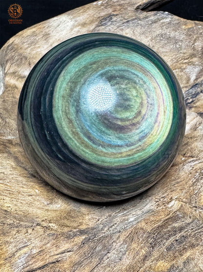 Sphère en obsidienne polie, œil décentré aux nuances jaune-vert et bleu clair, entouré de couronnes vertes et mauves.