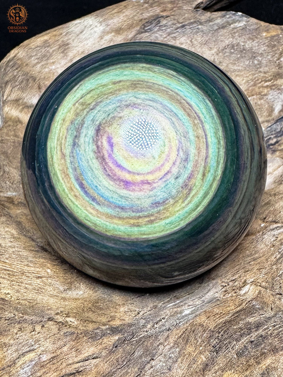 Sphère en obsidienne Manta Huichol aux reflets jaunes et vert d’eau, avec de fines bandes bleues et violettes concentriques.