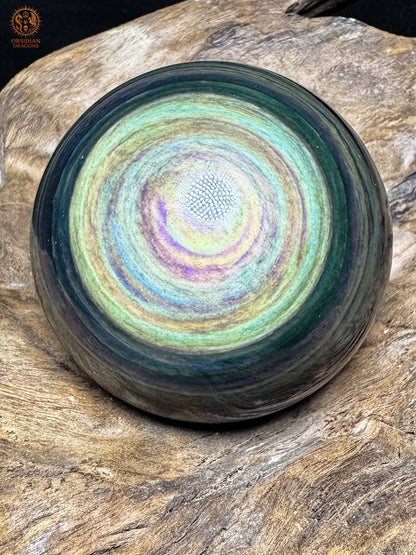 Sphère en obsidienne Manta Huichol aux reflets jaunes et vert d’eau, avec de fines bandes bleues et violettes concentriques.