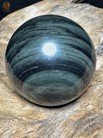 Vue latérale de la sphère en obsidienne naturelle, larges bandes ondulantes gris-vert sur la surface noire polie.