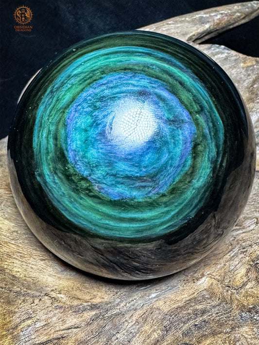 Sphère en obsidienne œil céleste Manta Huichol, au centre bleu lumineux entouré de bandes vertes et turquoise ondulantes - Obsidian Dragons