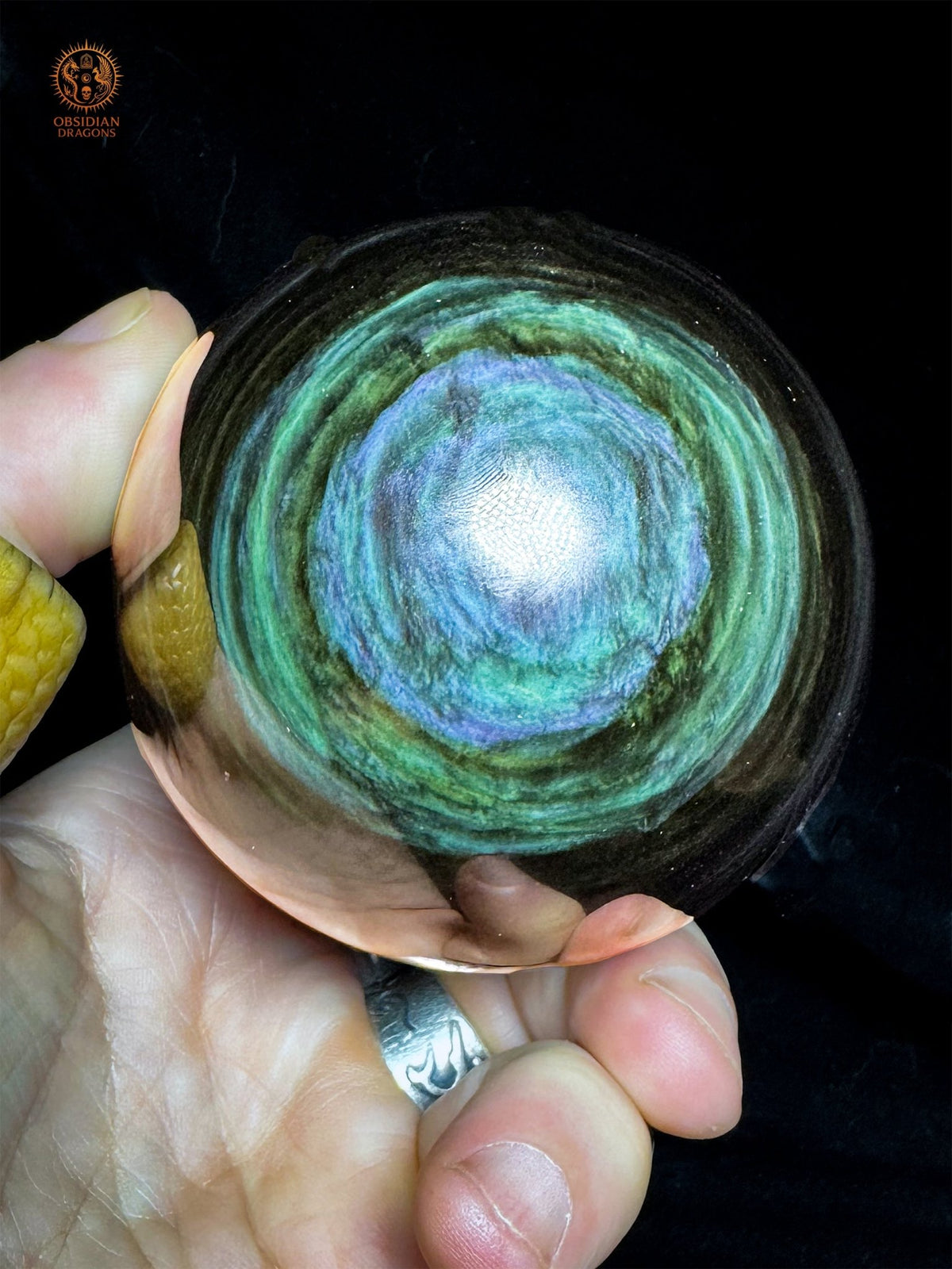 Sphère en obsidienne Manta Huichol du Mexique tenue en main, avec une plage bleu lavande irrégulière bordée de vert turquoise - Obsidian Dragons