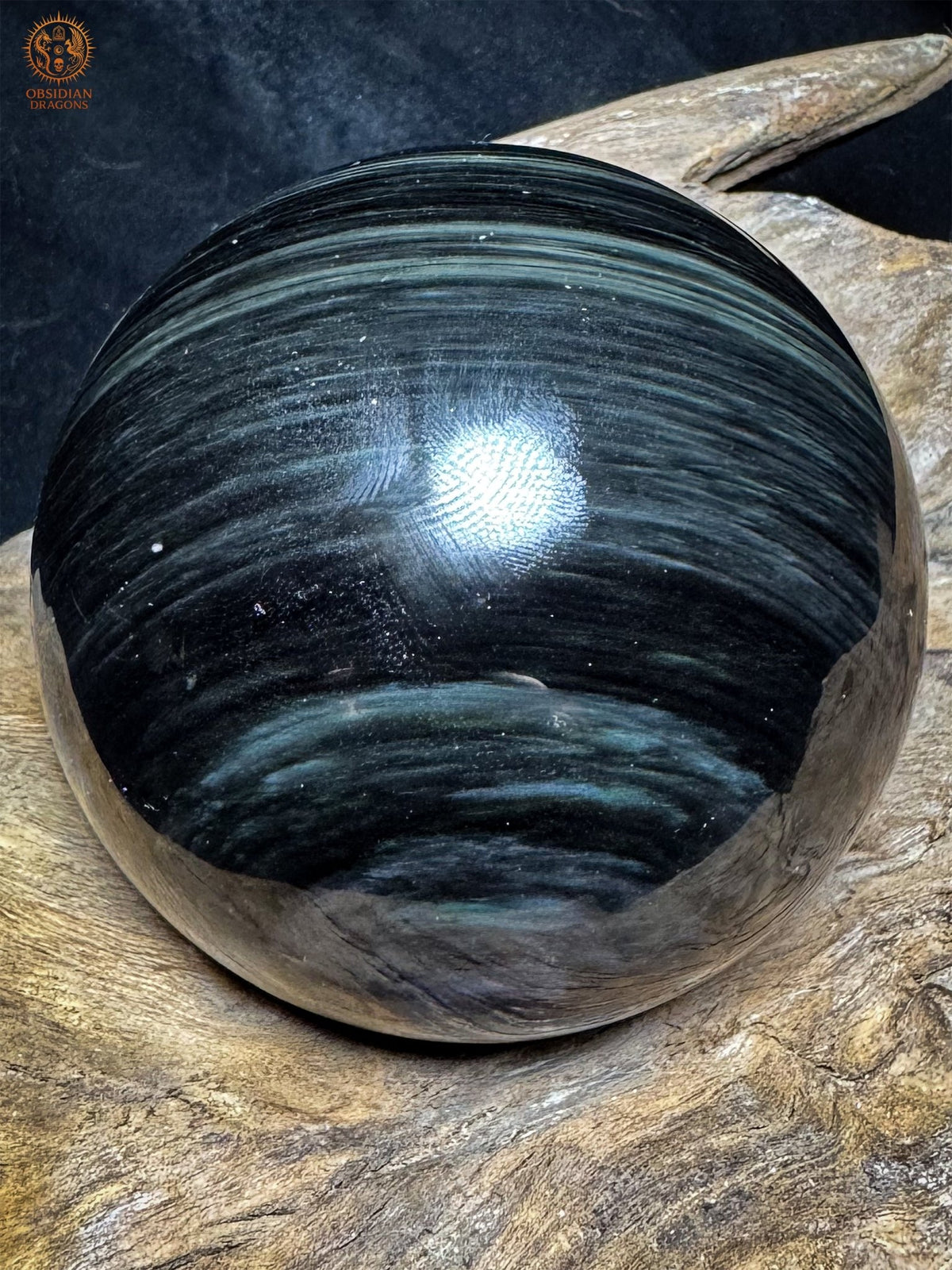 Sphère en obsidienne Manta Huichol sur bois, aux rubans bleu-gris ondulants et au motif ovale visible en partie basse.