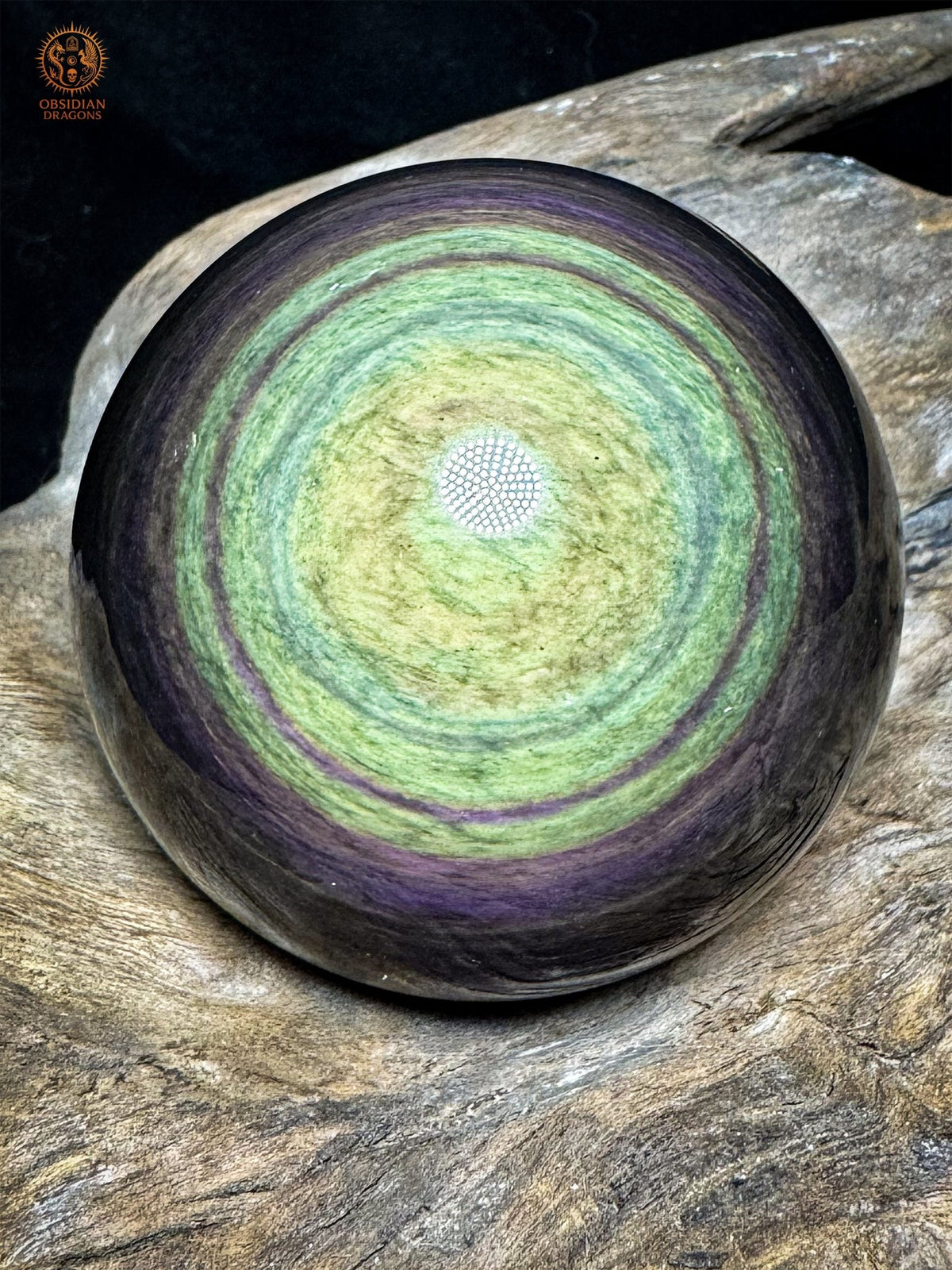 Sphère en obsidienne Manta Huichol du Mexique de 7 cm, centre jaune-vert entouré de couronnes vertes et violettes, posée sur bois - Obsidian Dragons
