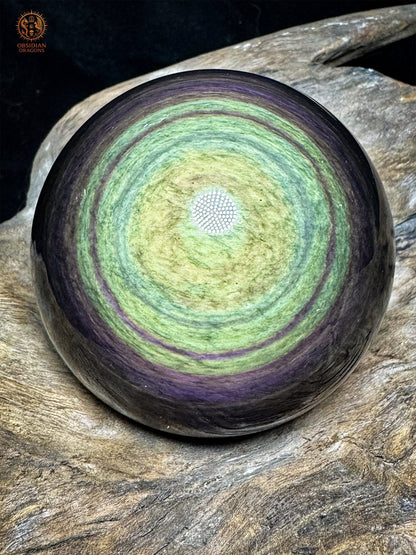 Sphère en obsidienne Manta Huichol du Mexique de 7 cm, centre jaune-vert entouré de couronnes vertes et violettes, posée sur bois - Obsidian Dragons
