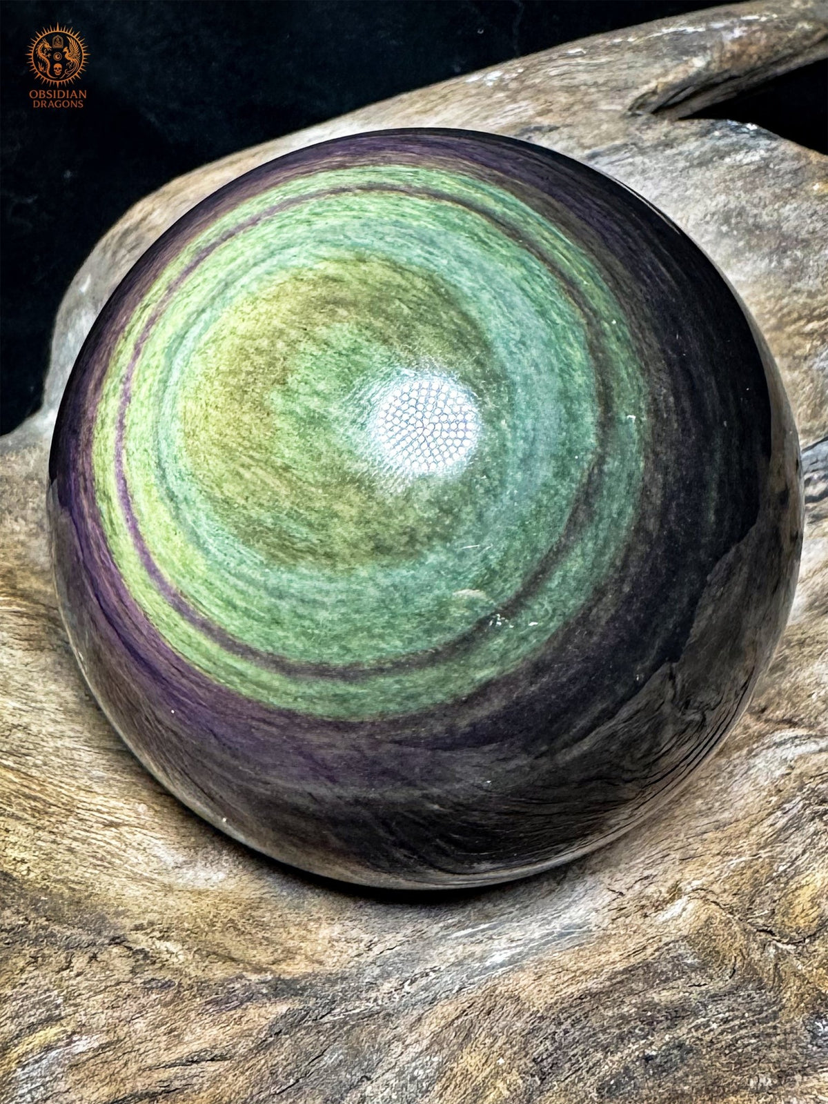 Sphère en obsidienne naturelle du Mexique vue de biais, reflets jaunes et vert turquoise bordés de couronnes violettes.