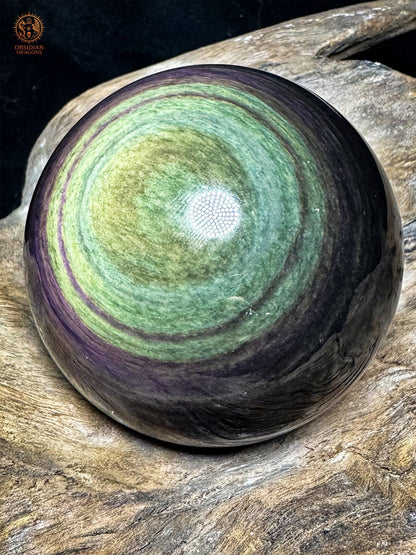 Sphère en obsidienne naturelle du Mexique vue de biais, reflets jaunes et vert turquoise bordés de couronnes violettes.