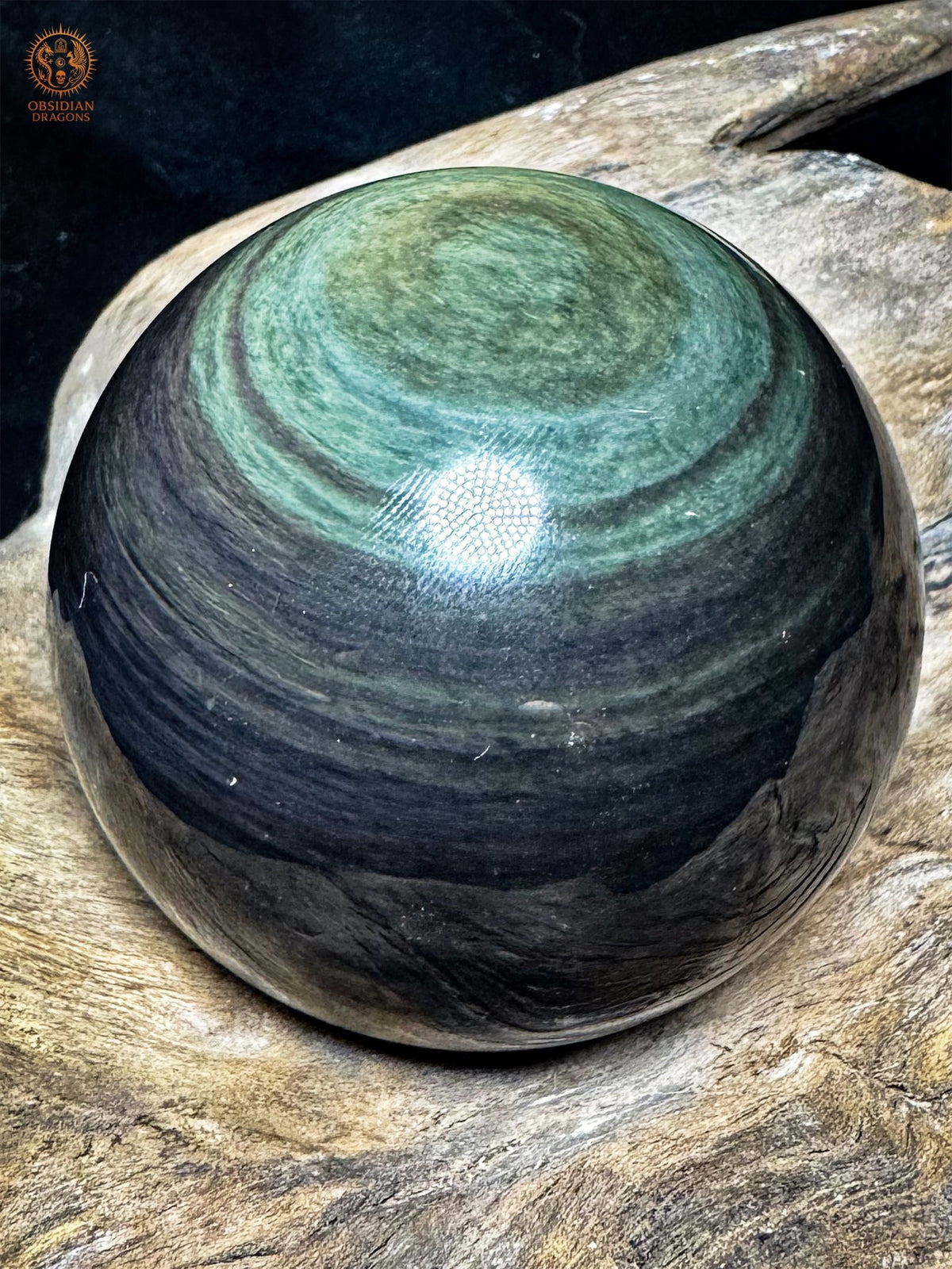 Sphère en obsidienne Manta Huichol vue de biais, couronnes vert turquoise et centre jaune-vert en partie haute, surface noire polie.